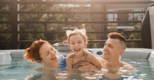 A mother and father are holding their young daughter in a spa pool, all three are smiling