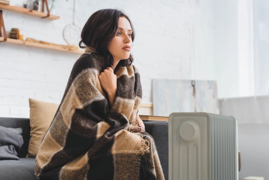 young woman wrapped in blanket by heater