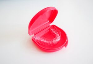 A clear aligner for orthodontic treatment stored in a red plastic case on a white surface.